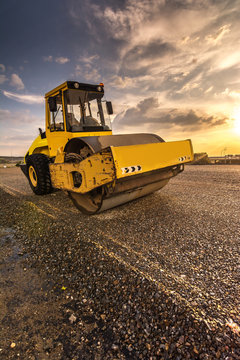 Yellow steamroller on asphalt road in sunlight