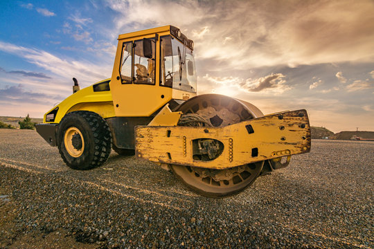 Yellow steamroller on asphalt road in sunlight