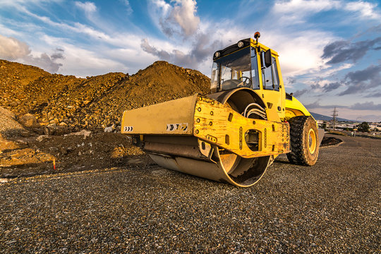 Yellow steamroller on asphalt road in sunlight