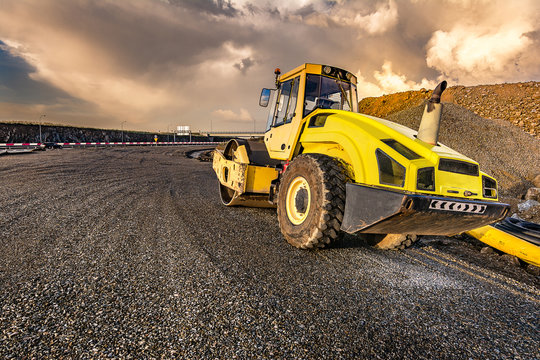 Yellow steamroller on asphalt road in sunlight