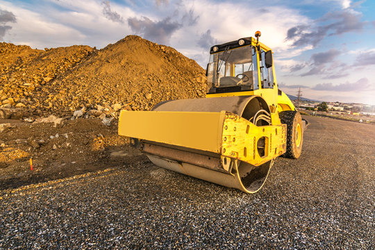 Yellow steamroller on asphalt road in sunlight