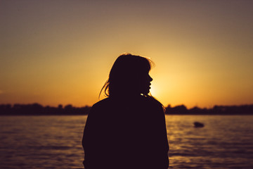 Silhouette of young woman sitting near the water on sand beach with sand in hands