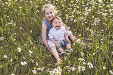 Cute child girl at camomile field daisy with baby brother