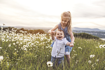 Cute child girl at camomile field daisy with baby brother