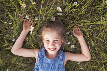 child on green daisy grass in a summer park sunset time
