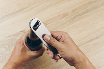 close up hand using a stainless steel bottle opener or bar blade to open a bottle of beer - obrazy, fototapety, plakaty