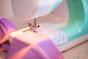 Tailoring process with sewing machine of mint blue colors, lavender cotton fabrics, white tissue in lilac and pink flowers are on wooden table.