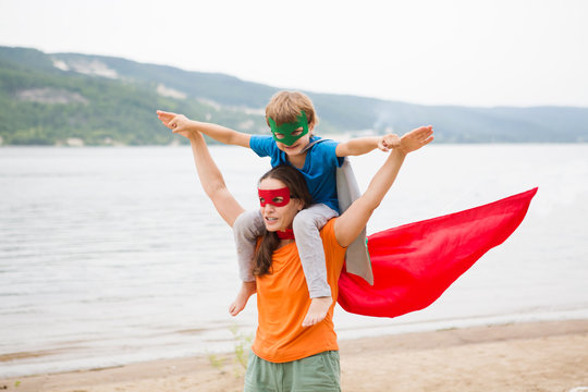 Child and mother playing superhero together and having fun outdoor. Concept of friendly family.