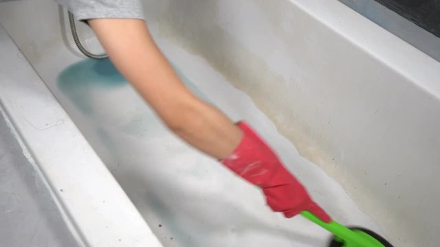 hand in gloves cleaning bathtub with brush