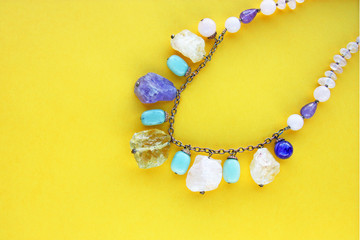 Template with copy space by top view closeup macro photo of a necklace of semi-precious stones (amethyst, rose quartz, quartz, lapis lazuli, blue agate) put on yellow paper. 