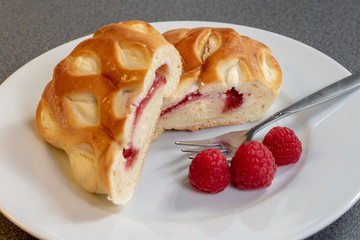 Ein Stück Himbeerkuchen dekoriert mit frischen Himbeeren auf einem weißen Kuchenteller