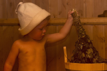 Beauty, healthcare. baby Boy relaxing in the sauna Toddler with broom and hat in russian sauna or...