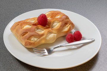 Ein braun gebackenes Teilchen dekoriert mit frischen Himbeeren auf einem weißen Kuchenteller