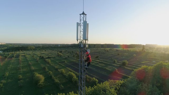 worker get down from the radio telecommunication tower with the help of belay on background of beautiful landscape
