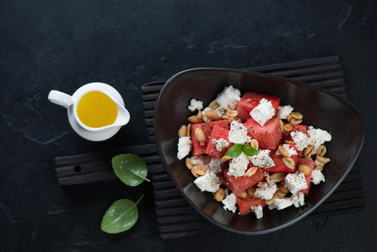 Salad with watermelon cubes, feta cheese, nuts and olive oil. View from above on a black stone background