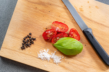 Tomaten halbiert mit Basilikumblatt, Salz und Pfeffer auf einem Holzbrett in der Küche