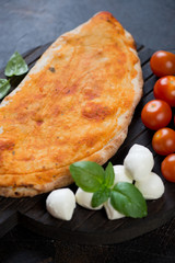 Closeup of italian pizza calzone with mozzarella, cherry tomatoes and green basil, vertical shot