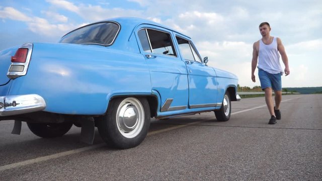 Girl is getting out of retro auto and running away with her boyfriend. Young man opens door of old car for his girlfriend. Woman coming out of vintage automobile. Leisure of happy couple. Slow Motion