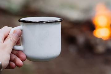 hands holding cup of tea the outdoors. Adventure, travel, tourism and camping concept. Hiker drinking tea from mug at camp
