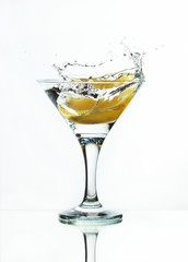 A glass of martini and slice of lemon, a splash and spray on a light background