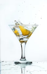 Foto op Plexiglas A glass of martini and slice of lemon, a splash and spray on a light background © fieryphoenix