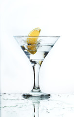 A glass of martini and slice of lemon, a splash and spray on a light background