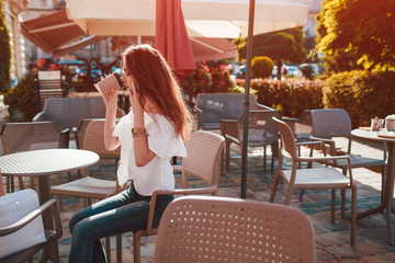 Beautiful stylish young woman with shopping bags chilling in outdoor cafe on city street and talking on phone.