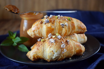 Croissants sprinkled with nuts and sugar powder. A jar of caramel in the background