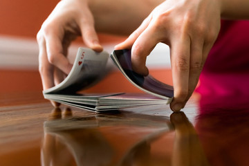 Person Shuffling a Deck of Cards on a Reflective Wooden Table