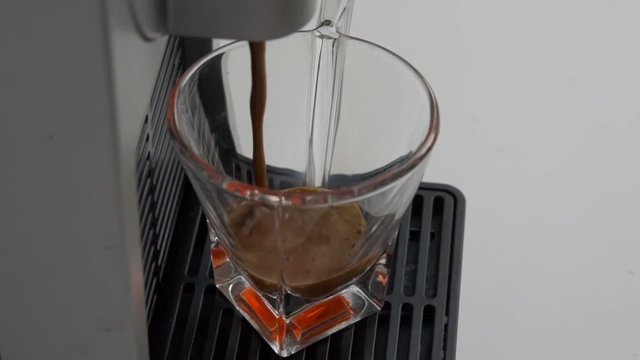 espresso coffee of the highest quality Italian made with a capsule coffee machine falls into a transparent glass coffee cup in slow motion 120 frame. concept of Italy, relax, bio and nature.
