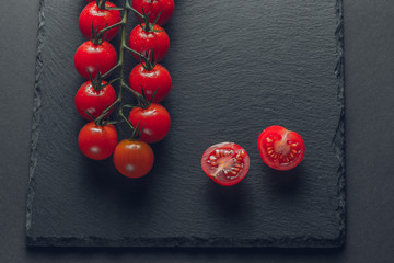 branch of fresh tomatoes cherry on a stone black background