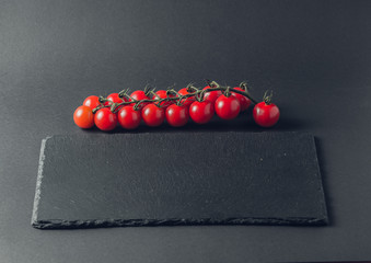 branch of fresh tomatoes cherry on a stone black background