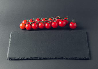 branch of fresh tomatoes cherry on a stone black background