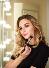  Portrait of make up artist woman with makeup brush near face. Beauty concept. Fashionable pretty girl with curly hair in beauty salon