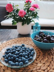 Berry mix in bowls on a table. Blueberries and sweet cherries in a beautiful bowls, roses and candleholder on a table. Side view. Summer, freshness.