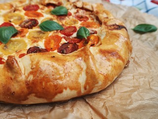 Tomato pie with fresh basil on a baking paper, pie on a cloth. Cherry tomato mix pie with cheese. Top view.