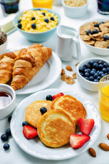 Breakfast table setting with flakes, juice, croissants, pancakes and fresh berries