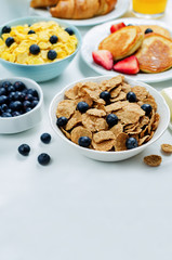 Breakfast table setting with flakes, juice, croissants, pancakes and fresh berries
