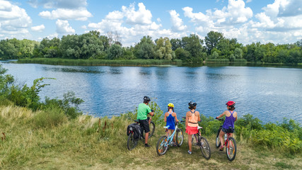 Family on bikes cycling outdoors, active parents and kids on bicycles, aerial view of happy family with children relaxing near beautiful river from above, sport and fitness concept
