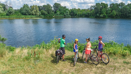 Family on bikes cycling outdoors, active parents and kids on bicycles, aerial view of happy family with children relaxing near beautiful river from above, sport and fitness concept
