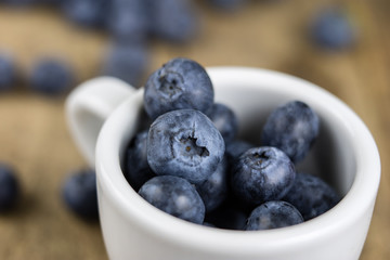 Ripe blueberry fruit in a container on a wooden kitchen table. Fruit prepared for dessert.
