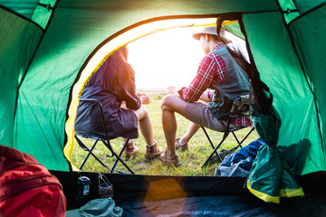Male and female campers talking each others in front of camping tent. People nad lifestyles concept. Picnic and travel concept. Nature in summer theme. Back view and inside of tent angle