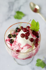 Creamy ice cream with red and black currants in a glass on a light table.