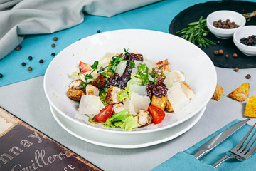 Caesar salad with chicken on blue background closeup view. Salad, spices and herbs, crackers.