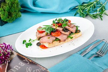 Bruschetta with roast beef on white plate. Blue background with knife and fork. 45 degree view.