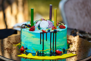 Blue buttercream birthday cake with colorful sprinkles over yellow background.