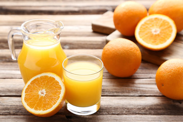 Orange fruit with jug and glass of juice on brown wooden table