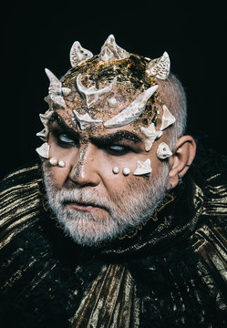Evil underworld king with thorns on face and white beard wearing dark metallic outfit isolated on black background. Demon head with angry look, fantasy concept