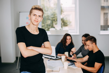 Fototapeta premium I am the part of cohesive team. Young successful man specialist portrait with colleagues meeting behind him. friendly atmosphere, communication and comradery