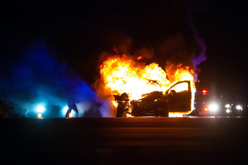 Car on fire at night with police lights in background